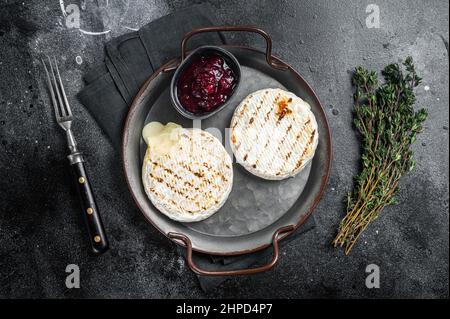 Gebackener Camembert-Käse auf einem Stahlblech mit Cranberry-Sauce und Thymian. Schwarzer Hintergrund. Draufsicht Stockfoto