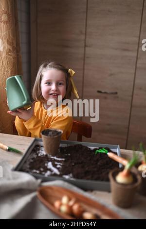 Konzept der Gartenarbeit. Kleines Mädchen ist bei der Pflanzung von Samen für Sämlinge beschäftigt, Gießen Erde in Töpfe für den Anbau von Kulturen. Stockfoto