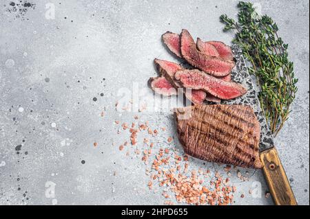 Braten Sie in Scheiben geschnittene Flanke oder Flap Steak auf einem Metzgerspalter mit Thymian und rosafarbenem Salz. Grauer Hintergrund. Draufsicht. Speicherplatz kopieren Stockfoto