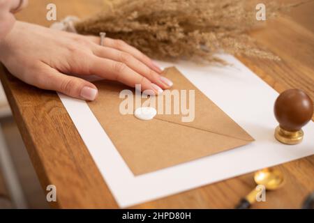 Cropped Foto Frau Hand Herstellung Grußkarte Papier Umschlag handgefertigt, Handwerk auf Holz Schreibtisch, Versiegelung Wachs Print Gummi. Stockfoto