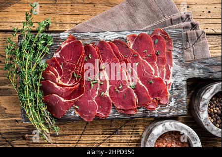 Getrocknete Pastrami-Scheiben, Rinderfleisch mit Kräutern auf Holzbrett. Holzhintergrund. Draufsicht Stockfoto