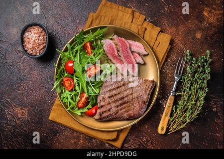 Geröstete Flanke oder Flap Steak auf einem Teller mit Salat. Dunkler Hintergrund. Draufsicht Stockfoto