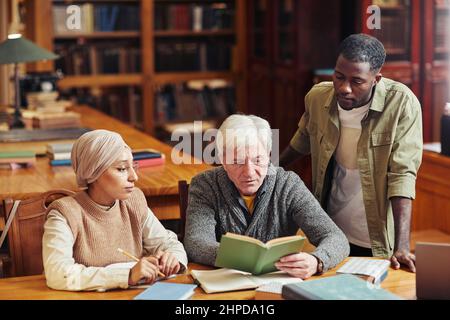 Porträt eines weißhaarigen älteren Mannes, der mit zwei jungen Studenten in der Bibliothek studiert Stockfoto
