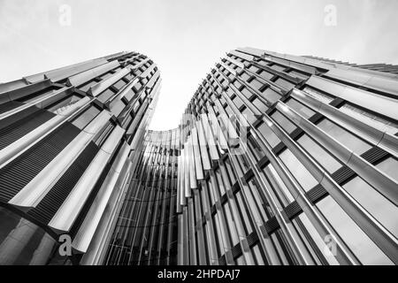 Schwarz-weißes Hochhaus des Metropolenzentrums von unten. Nahaufnahme der modernen städtischen Gebäudefassade und des Himmels in der Innenstadt. Künstlerische Details. Stockfoto