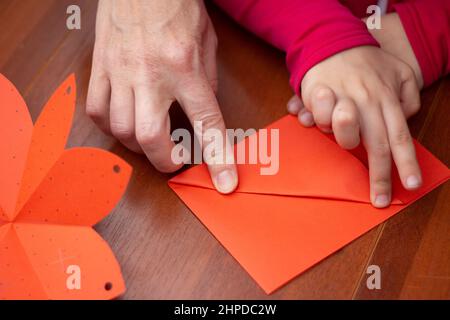 Faltpapier. Unterricht in der Kreativität von Kindern. Kinder und Erwachsene gestalten zusammen einen Umschlag. Co-Creation. Origami-Hintergrund wird ausgeführt. Stockfoto