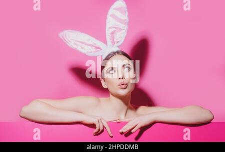 Ostern junge Frau Studio trägt Hasenohren. Neugierig isoliert auf rosa. Stockfoto