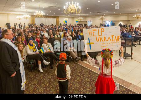 Warren, Michigan, USA. 20th. Februar 2022. Das ukrainisch-amerikanische Krisenreaktionskomitee hält eine „Haltung zur Ukraine“-Kundgebung ab, während die Bewohner die Folgen einer möglichen russischen Invasion dieses Landes fürchten. Fast 40.000 Einwohner von Michigan sind ukrainischer Abstammung. Ksenia Zagaiko, 8, hält ein Schild mit der Aufschrift „Hilf der Ukraine“. Pfarrer Daniel Schajkoski, Pfarrer der Ukrainischen Katholischen Kirche der Unbefleckten Empfängnis, ist links. Kredit: Jim West/Alamy Live Nachrichten Stockfoto