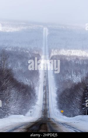 Uebec 216 Straße, in der Region Chaudière-Appalaches, im Winter mit einem großen Panoramablick auf den verschneiten Wald, der an die teilweise verschneite Straße grenzt. Stockfoto