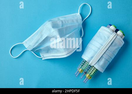 Insulin-Spritzenstifte mit medizinischen Masken auf blauem Hintergrund Stockfoto