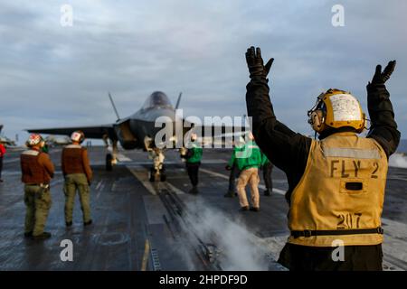 PHILIPPINISCHES MEER (Feb 19, 2022) Aviation Boatswain's Mate (Handling) 2nd Class Devin Reynoso aus Port Hueneme, Kalifornien, leitet einen F-35C Lightning II, der den 'Black Knights' of Marine Fighter Attack Squadron (VMFA) 314 zugewiesen wurde, auf dem Flugdeck des Flugzeugträgers USS Abraham Lincoln (CVN 72) der Nimitz-Klasse. Die Abraham Lincoln Strike Group befindet sich im geplanten Einsatzgebiet der US-Flotte für 7th, um die Interoperabilität durch Allianzen und Partnerschaften zu verbessern und gleichzeitig als reaktionsfähige Truppe zur Unterstützung einer freien und offenen Region im Indo-Pazifik-Raum zu dienen. (USA Navy Foto von Mass Communi Stockfoto