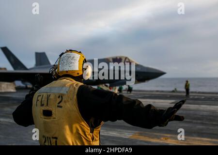 PHILIPPINISCHES MEER (Feb 19, 2022) Aviation Boatswain's Mate (Handling) 2nd Class Devin Reynoso aus Port Hueneme, Kalifornien, leitet einen F-35C Lightning II, der den 'Black Knights' of Marine Fighter Attack Squadron (VMFA) 314 zugewiesen wurde, auf dem Flugdeck des Flugzeugträgers USS Abraham Lincoln (CVN 72) der Nimitz-Klasse. Die Abraham Lincoln Strike Group befindet sich im geplanten Einsatzgebiet der US-Flotte für 7th, um die Interoperabilität durch Allianzen und Partnerschaften zu verbessern und gleichzeitig als reaktionsfähige Truppe zur Unterstützung einer freien und offenen Region im Indo-Pazifik-Raum zu dienen. (USA Navy Foto von Mass Communi Stockfoto