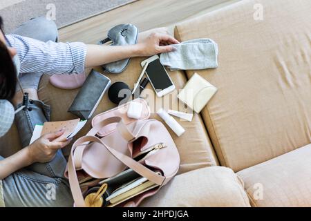 Draufsicht Frau, die sich auf den Flug vorbereitet, indem sie verschiedene persönliche Dinge in die Handtasche legt Stockfoto