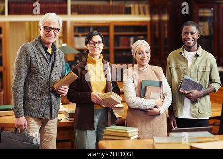 Eine vielfältige Gruppe von Menschen, die Bücher in der klassischen Bibliothek halten und die Kamera betrachten Stockfoto