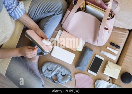 Draufsicht Frau, die sich auf den Flug vorbereitet, indem sie verschiedene persönliche Dinge in die Handtasche legt Stockfoto