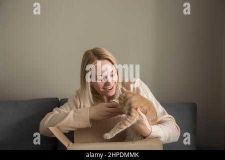 Glückliches Mädchen mit blonden langen Haaren, die ein Geschenk halten, ein Kätzchen, das ein Geburtstagsgeschenk gab, in einer Geschenkbox, ein Geburtstagsgeschenk. Stockfoto