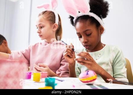 Kinder malen Ostereier und tragen Hasenohren, während sie in der Schule Kunst- und Bastelunterricht genießen Stockfoto