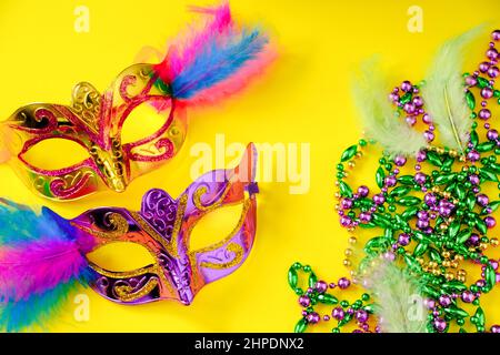 Zwei mehrfarbige Karnevalsmasken und Perlen auf gelbem Hintergrund. Mardi Gras Konzept. Fat Tuesday-Symbol. Festliche Dekorationen aus nächster Nähe. Stockfoto