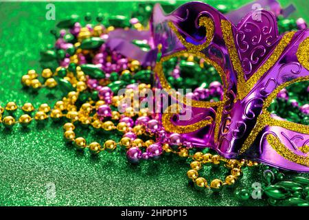 Karnevalsmaske und bunte Perlen auf grün glänzendem Hintergrund. Mardi Gras Konzept. Fat Tuesday Symbol Nahaufnahme. Festlich glänzende Dekorationen in Gold, gree Stockfoto