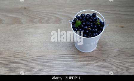 Eimer mit amerikanischen Blaubeeren in einem weißen Eimer auf einem Holztisch Stockfoto