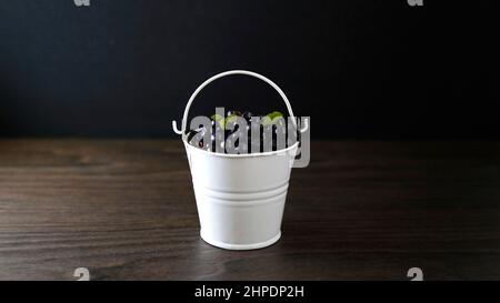 Eimer mit amerikanischen Blaubeeren in einem weißen Eimer auf schwarzem Holzhintergrund Stockfoto