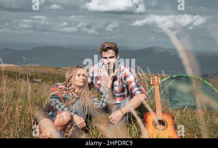 Glückliche Paar Touristen Mann und Frau, die eine Pause neben Lager, Gitarre und sonnigen Tag. Reisepaar genießen Fernweh Blick, Freunde Aufregung an Stockfoto