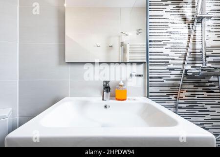 Weißes Waschbecken aus Steingut neben einem Duschschirm in einer Toilette einer Ferienwohnung Stockfoto