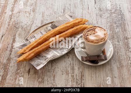 Spanisches Frühstück mit Kaffee mit Milch und ein paar porras auf einem eingelegten Holztisch Stockfoto