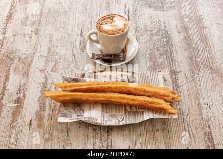 Spanisches Frühstück aus der Gegend von Madrid mit Kaffee mit Milch und ein paar porras auf einem eingelegten Holztisch Stockfoto