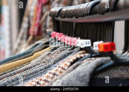 Schwarze Kleiderbügel mit Kleidungsstücken verschiedener Größen, die am Kleiderbügel eines Ladens hängen Stockfoto