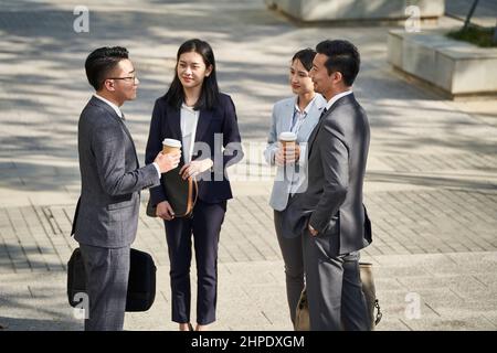 Gruppe von vier jungen asiatischen Geschäftsleuten, die draußen auf der Straße plaudern Stockfoto