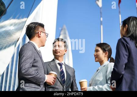 Gruppe von vier jungen asiatischen Geschäftsleuten, die draußen auf der Straße plaudern Stockfoto