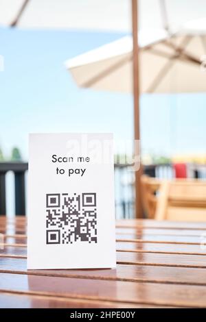 QR-Code für kontaktloses, bargeldloses Bezahlen, platziert auf dem Tisch einer Restaurantterrasse. Vertikales Bild mit Kopierbereich. Stockfoto