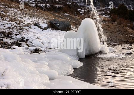 Ein Eisblock und ein Wasserstrom, der darauf fließt, vor der Kulisse eines wunderschönen Flusses, der von schneebedeckten Winterbergen umgeben ist. Altai, Siberi Stockfoto