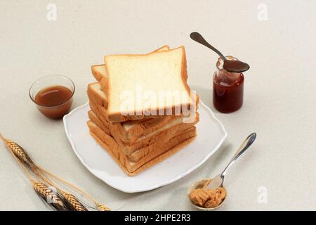 Toastbrot mit Laib (Shokupan oder Roti Tawar) zum Frühstück auf Holzboden, serviert mit Marmelade und Erdnussbutter. Bäckerkonzept Bild Stockfoto