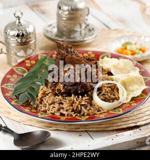 Nasi Kebuli (Kabuli-Reis), arabischer oder indischer Pilaf mit Rinderrippen oder Lamm, auf Holztisch. Serviert mit türkischem Tee Stockfoto