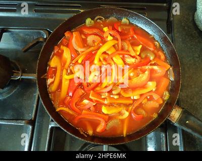 Rote und gelbe Paprika (Paprika) bilden die Grundlage dieses sommerlichen Gemüsegerichtes, das in einer großen Fritte auf einem Gaskochfeld köcheln lässt Stockfoto