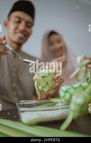 muslim paar asiatische Herstellung Ketupat Reiskuchen zu Hause mit Palmblatt Stockfoto