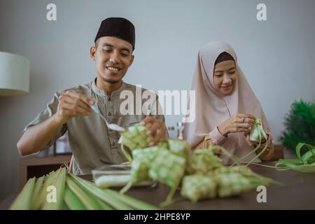 muslim paar asiatische Herstellung Ketupat Reiskuchen zu Hause mit Palmblatt Stockfoto