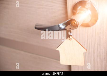 Schlüssel mit Schlüsselbund in Form Haus in Türschloss.mit hellem Sonnenlicht Stockfoto