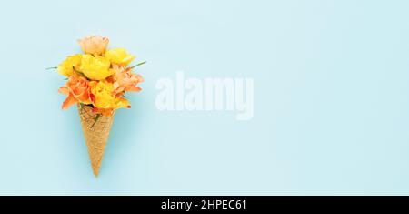 Gelbe Rosen in einem Waffel-Eis-Kegel auf blauem Hintergrund. Muttertag, Valentinstag, Bachelorette, Sommerkonzept Stockfoto