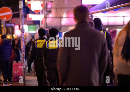 Hamburg, Deutschland. 20th. Februar 2022. Auf der Reeperbahn laufen Polizeibeamte zwischen Partygängern. In Hamburg trat am Samstag die erste Stufe der dreistufigen Aufhebung aller von Bund und Ländern geplanten Corona-Maßnahmen in Kraft. Geimpfte und wiedergeborene Menschen können sich seit Mitternacht wieder in unbegrenzter Zahl privat treffen. Außerdem wurden das Verbot des Alkoholverkaufs für Einzelhändler und die Ausgangssperre in Restaurants aufgehoben. Quelle: Jonas Walzberg/dpa/Alamy Live News Stockfoto