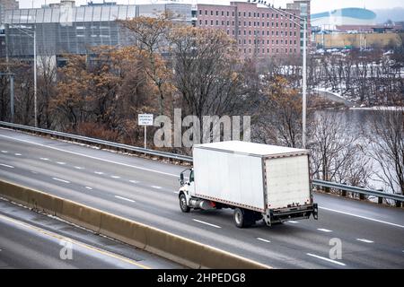Mittelstrom-Industrie-Tagestab-Sattelschlepper mit langem Boxanhänger, der kommerzielle Ladung transportiert, die auf der geteilten Winterautobahn entlang der ri verläuft Stockfoto