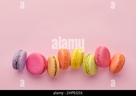 Bunte leckere französische Dessert-Makronen oder Makronen in einer Reihe auf rosa Hintergrund. Draufsicht mit Kopierbereich. Stockfoto