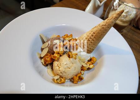 Nahaufnahme Schokolade und Vanille Eiscreme Waffelkegel serviert mit Karamell-Popcorn und Mandelscheiben Stockfoto