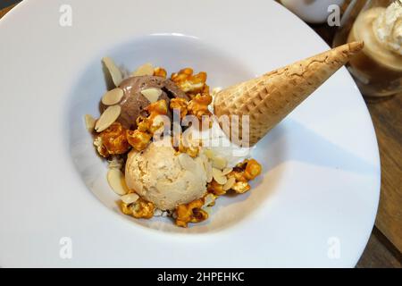 Nahaufnahme Schokolade und Vanille Eiscreme Waffelkegel serviert mit Karamell-Popcorn und Mandelscheiben Stockfoto