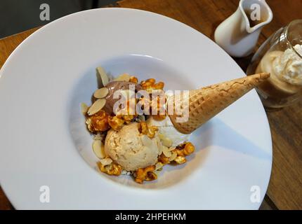 Nahaufnahme Schokolade und Vanille Eiscreme Waffelkegel serviert mit Karamell-Popcorn und Mandelscheiben Stockfoto