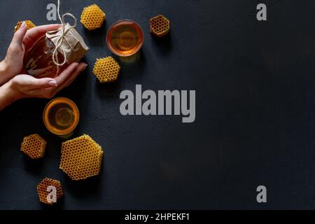 Hände einer Frau, die ein Glas mit Bienenhonig auf schwarzem Hintergrund hält. Speicherplatz kopieren. Stockfoto