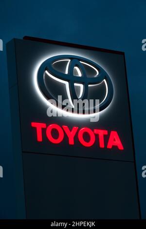 Batumi, Georgia - Januar 26 2022: Nahaufnahme des Toyota-Händlerlogos, das abends vor einem dunkelblauen Himmel beleuchtet wird. Vertikales Foto Stockfoto