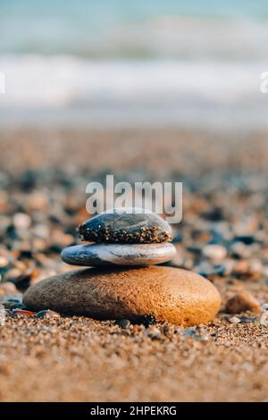 Felsbalancierung am Meeresstrand. Kieselsteinpyramide an sandigen Ufern. Stabiler Stapel oder Haufen im weichen Fokus mit Bokeh, Nahaufnahme. Zen-Balance, Minimalismus Stockfoto