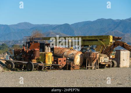 Alte verlassene Arbeitstransporte vor dem Hintergrund von Bergen an einem sonnigen Tag. Alte, rostige Arbeitsgeräte Stockfoto